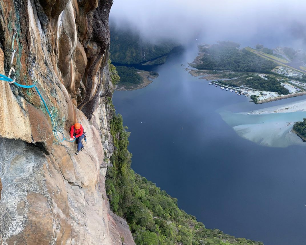 Climber on orange granite above fiord.